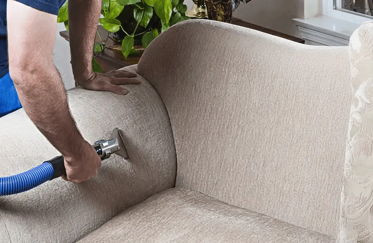 Professional upholstery cleaner deep-cleaning a fabric sofa with a handheld extraction tool and hose, Oklahoma City, OK.